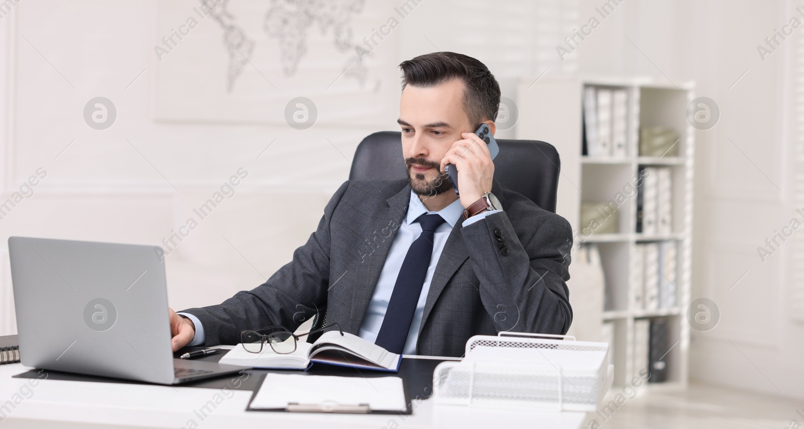 Photo of Handsome banker talking on smartphone at table in office