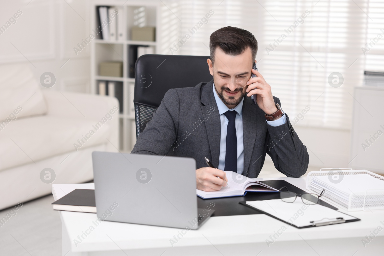 Photo of Happy banker talking on smartphone at table in office