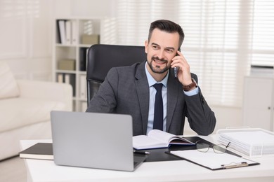 Photo of Happy banker talking on smartphone at table in office