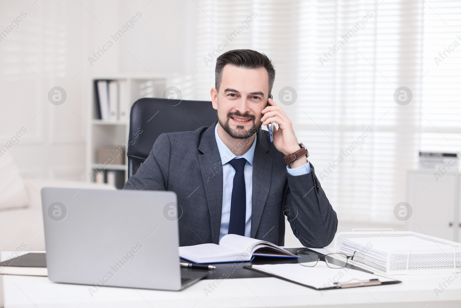 Photo of Happy banker talking on smartphone at table in office