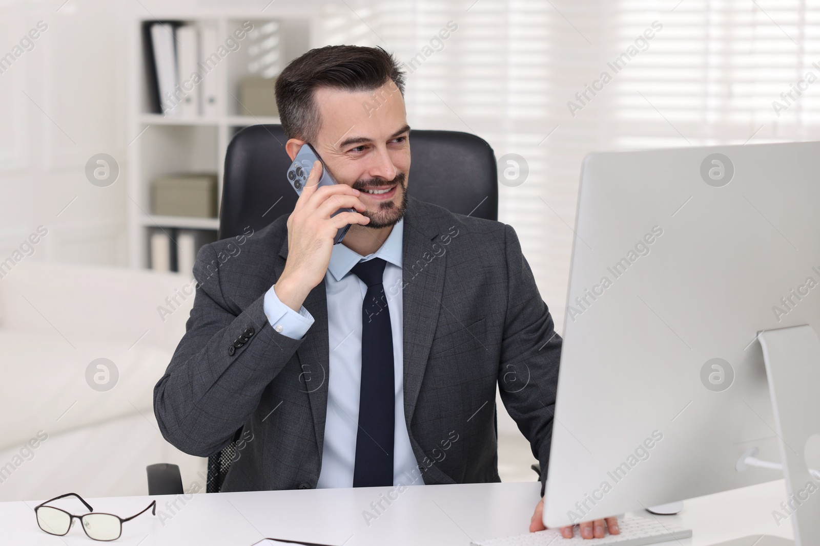 Photo of Happy banker talking on smartphone at table in office