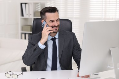 Photo of Happy banker talking on smartphone at table in office