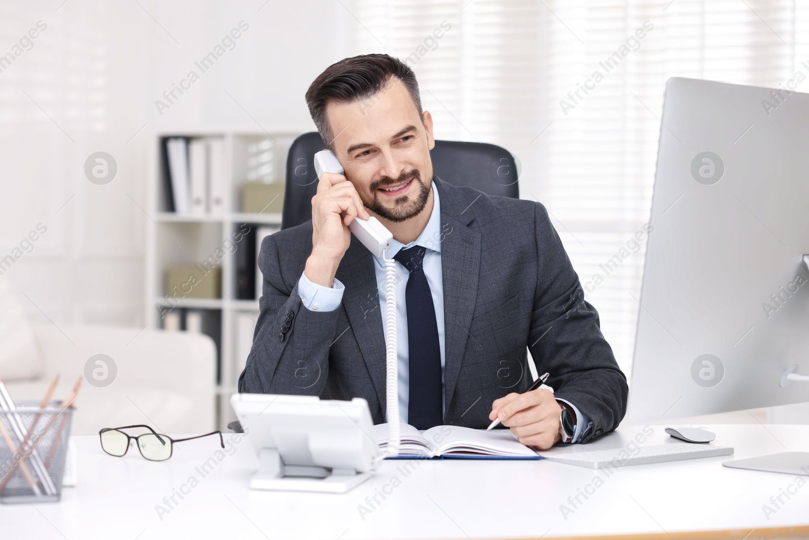 Photo of Happy banker talking on phone at table in office