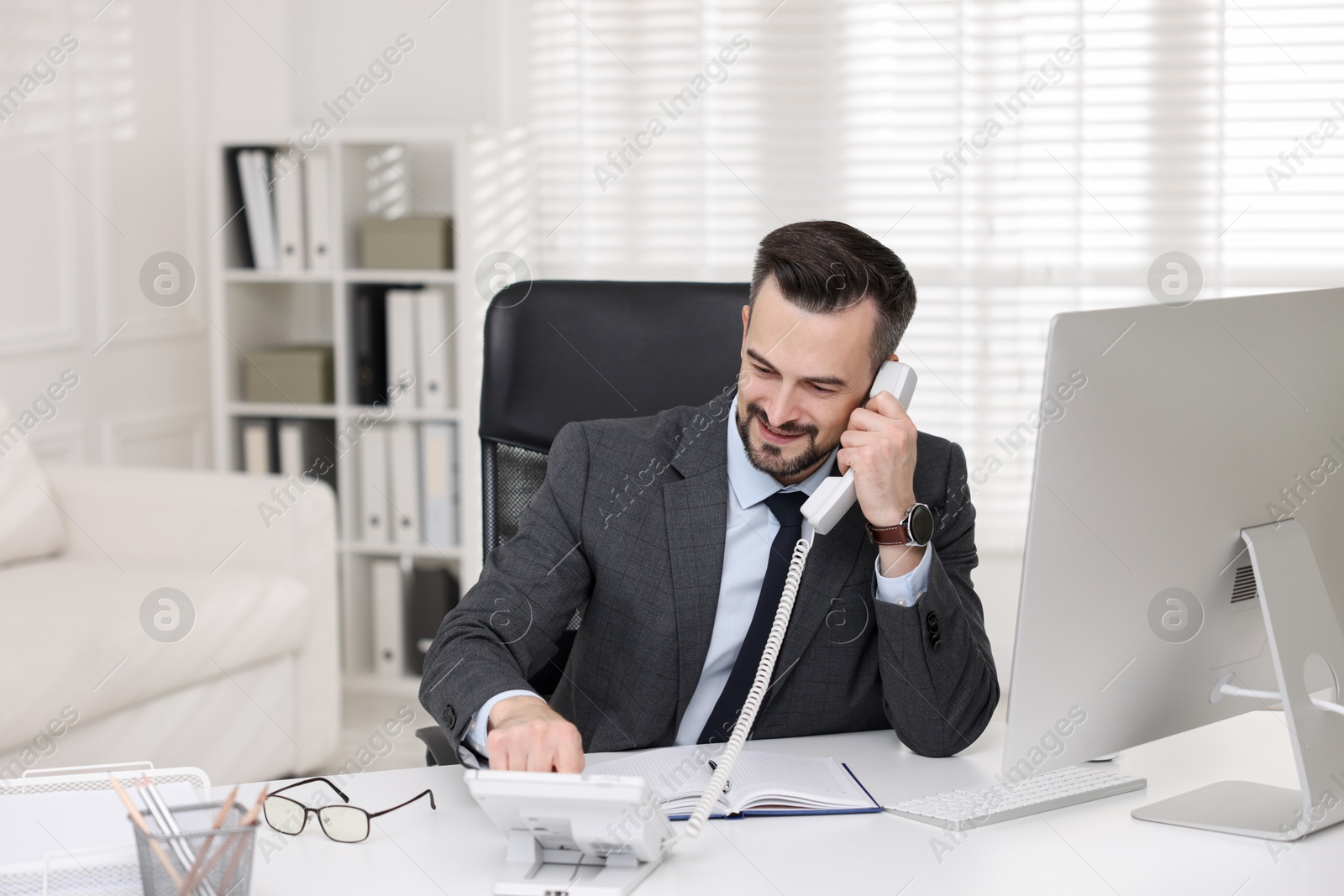 Photo of Happy banker talking on phone at table in office