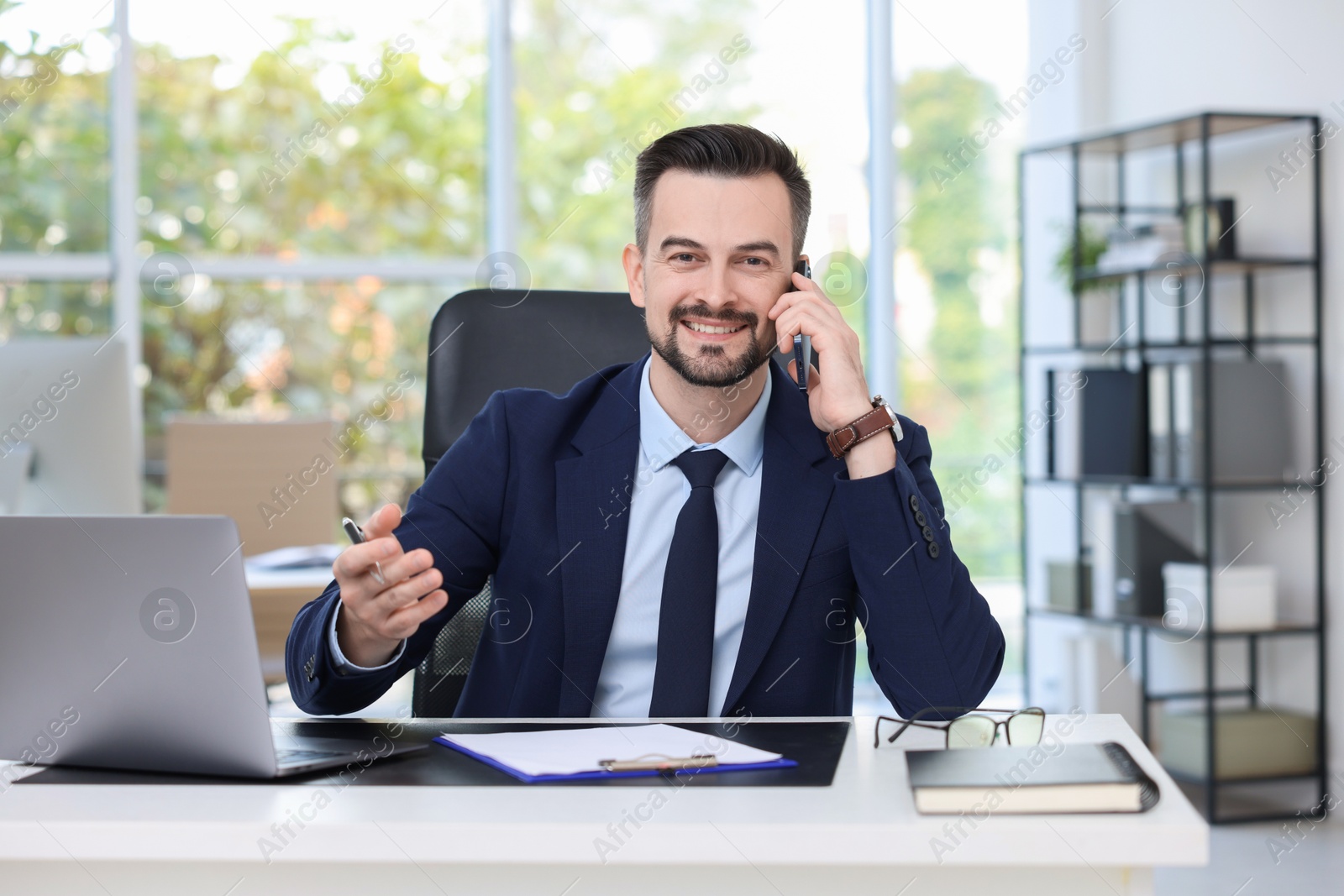 Photo of Happy banker talking on smartphone at table in office