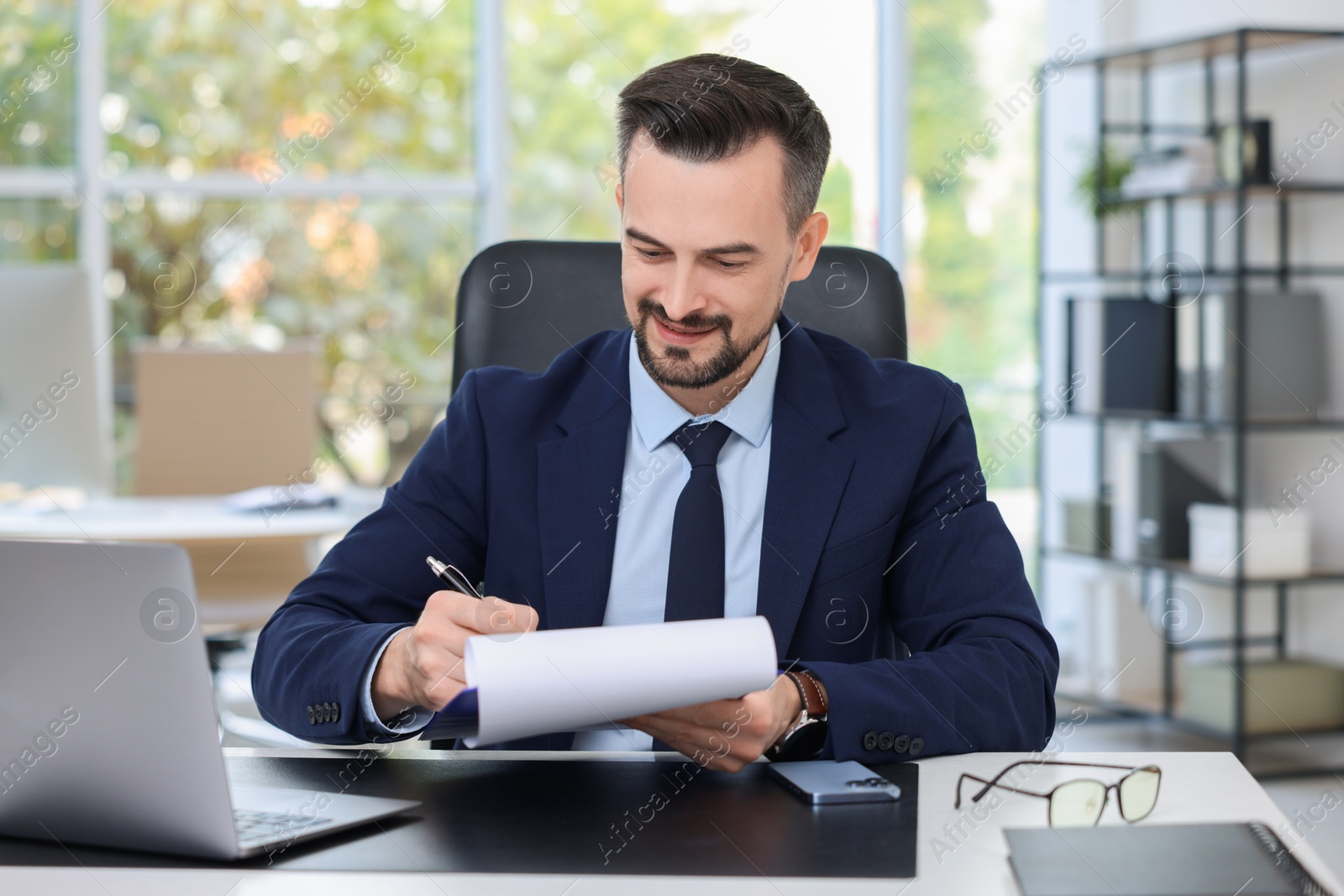 Photo of Handsome banker making notes at table in office