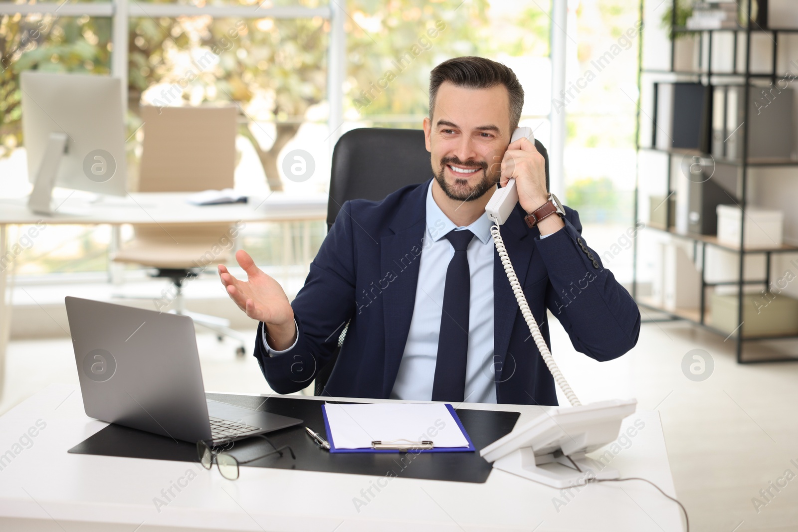 Photo of Happy banker talking on phone at table in office