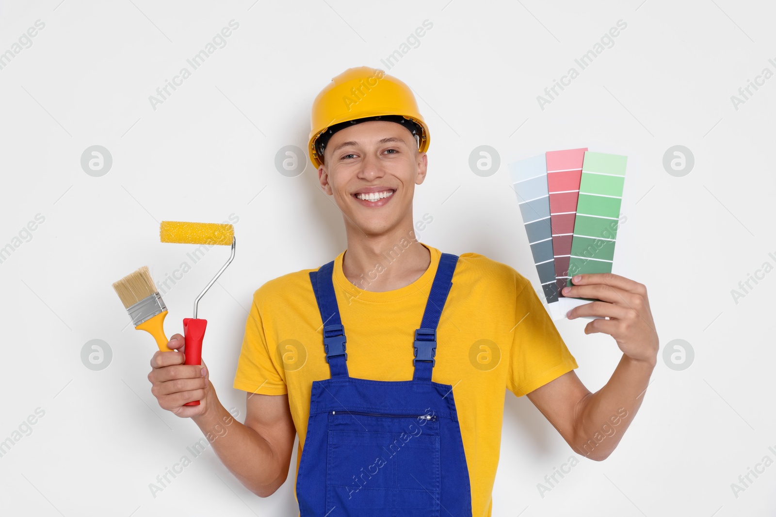 Photo of Portrait of young decorator with paint roller, color palettes and brush on white background