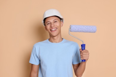 Photo of Portrait of young decorator with paint roller on beige background