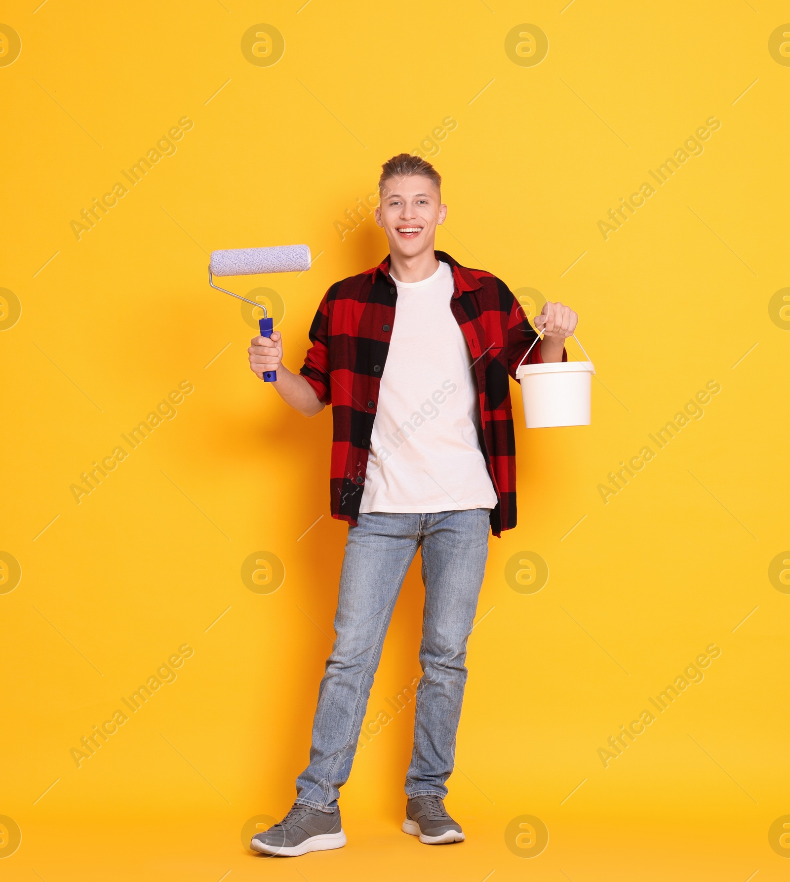 Photo of Young decorator with paint roller and bucket on orange background