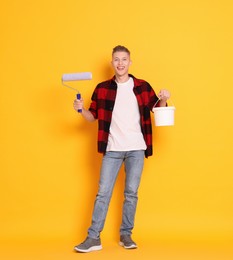 Photo of Young decorator with paint roller and bucket on orange background