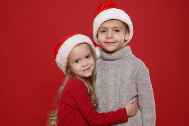 Photo of Cute little kids in Santa hats on red background