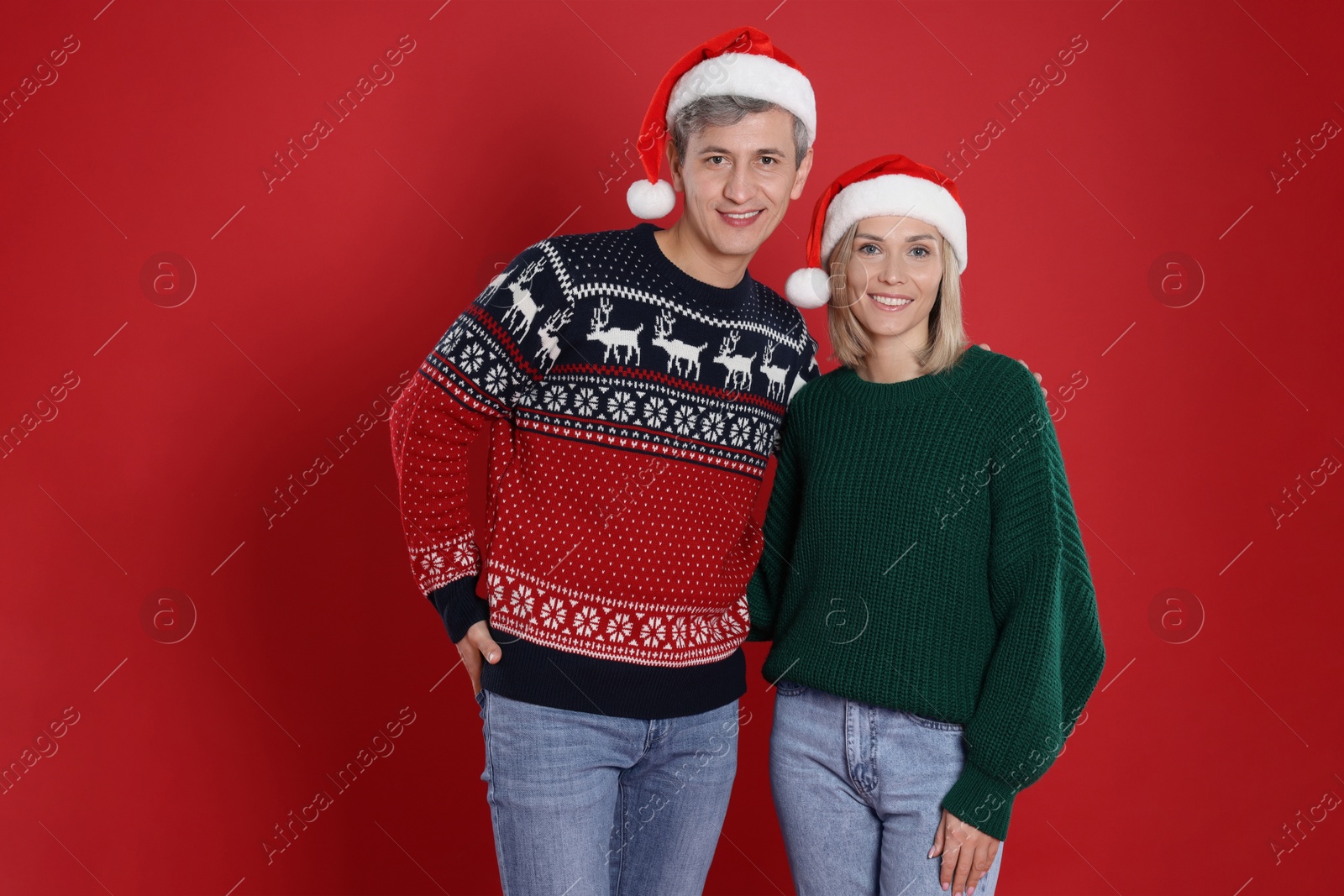 Photo of Happy couple in Santa hats on red background. Christmas celebration