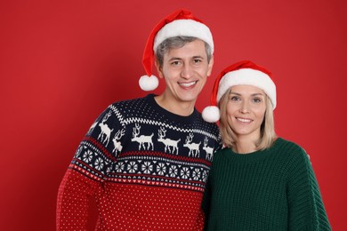 Photo of Happy couple in Santa hats on red background. Christmas celebration