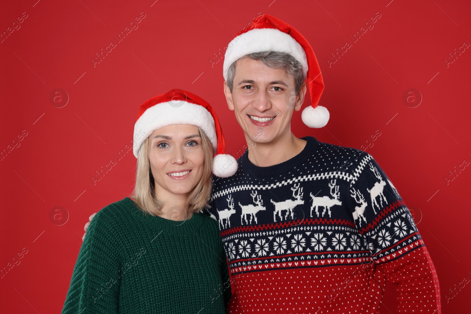 Photo of Happy couple in Santa hats on red background. Christmas celebration