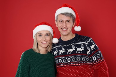 Photo of Happy couple in Santa hats on red background. Christmas celebration