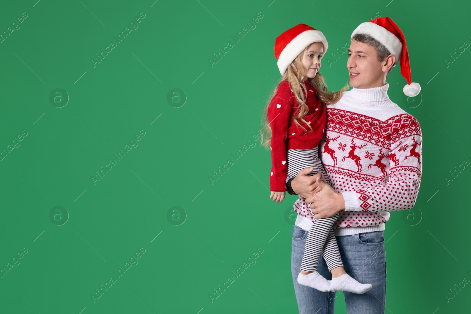 Photo of Father and daughter in Santa hats on green background, space for text. Christmas celebration