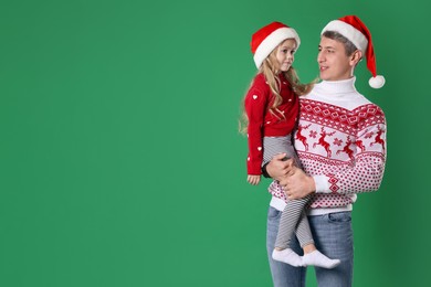 Photo of Father and daughter in Santa hats on green background, space for text. Christmas celebration