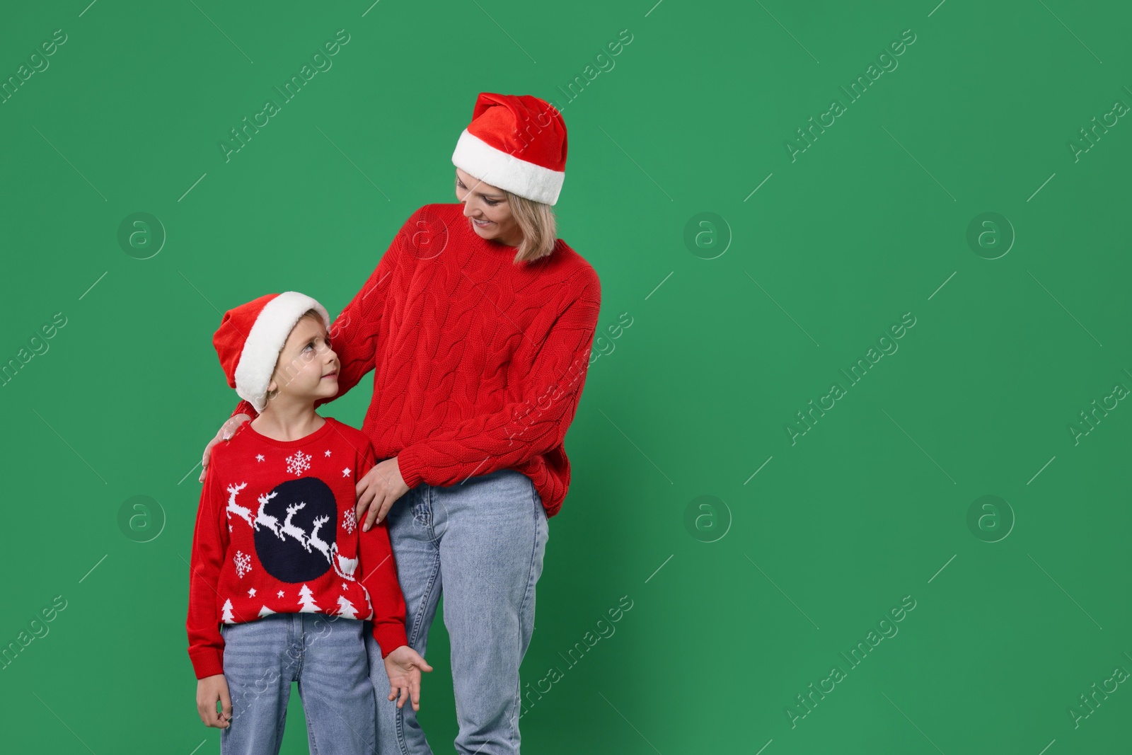 Photo of Mother and son in Santa hats on green background, space for text. Christmas celebration