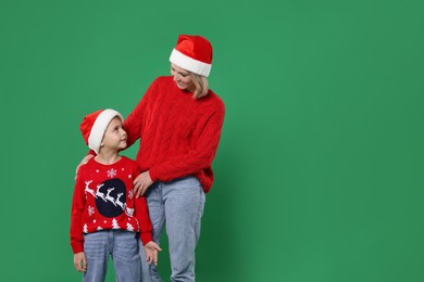 Photo of Mother and son in Santa hats on green background, space for text. Christmas celebration