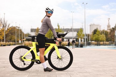 Photo of Young athletic woman with helmet and bicycle outdoors, space for text