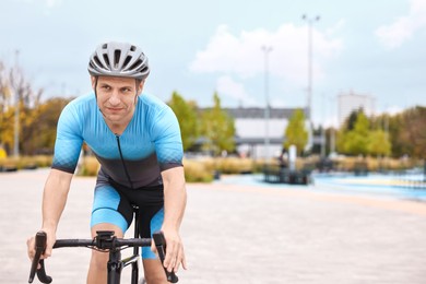 Photo of Athletic man with helmet riding bicycle outdoors, space for text