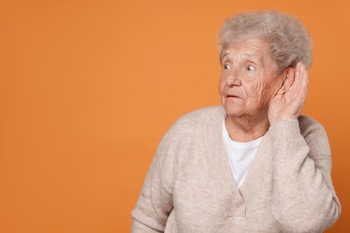 Photo of Senior woman showing hand to ear gesture on dark yellow background, space for text