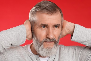 Photo of Senior man covering his ears on red background