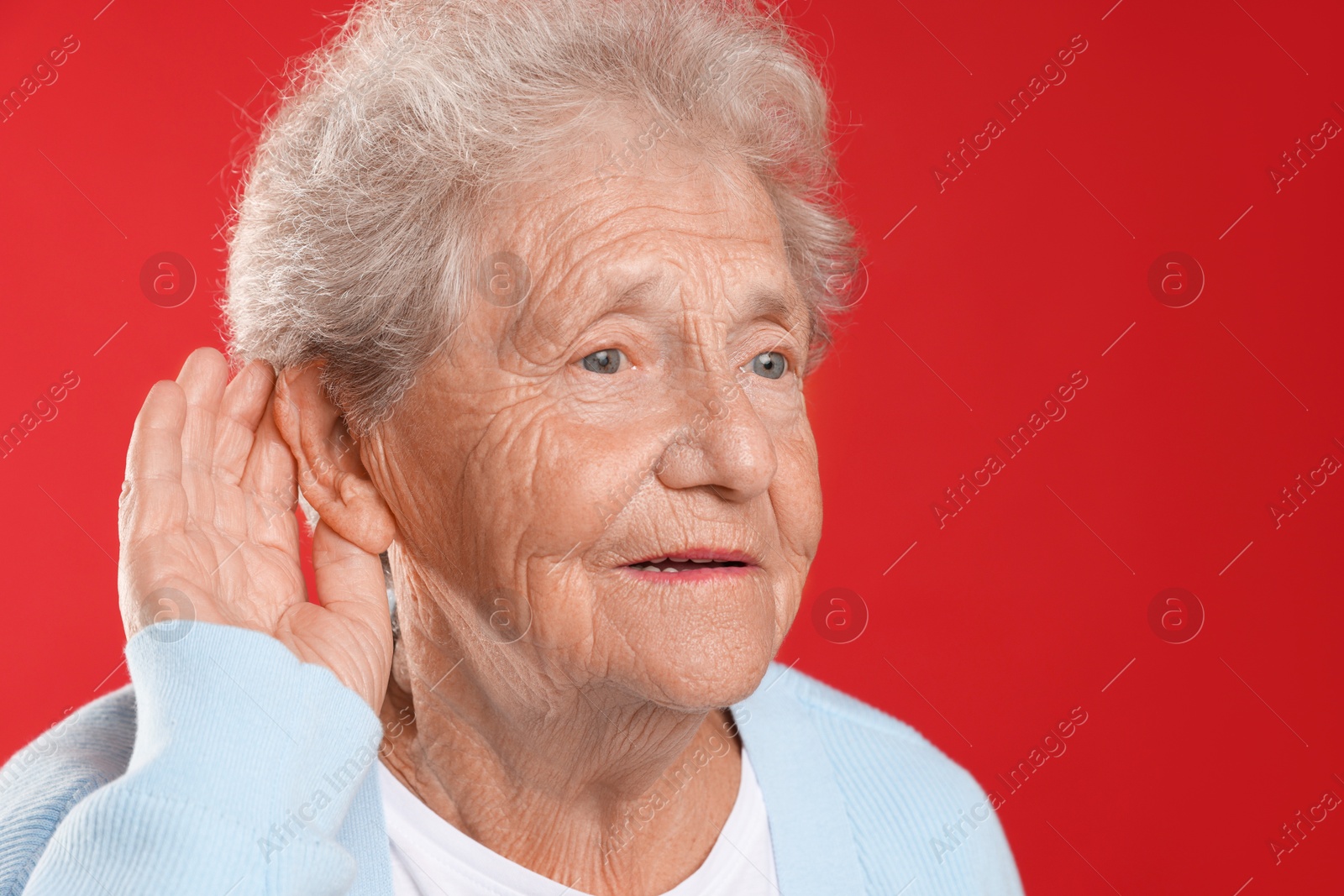 Photo of Senior woman showing hand to ear gesture on red background. Space for text