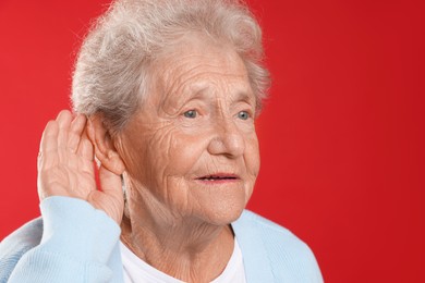 Photo of Senior woman showing hand to ear gesture on red background. Space for text