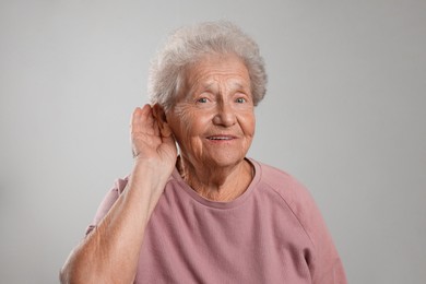 Photo of Senior woman showing hand to ear gesture on grey background