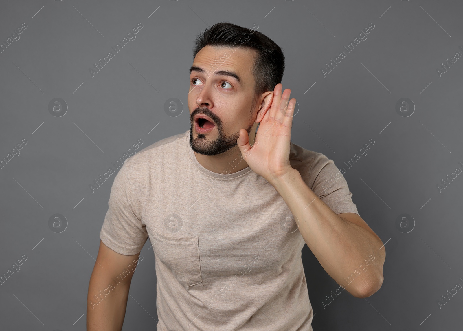 Photo of Man showing hand to ear gesture on grey background