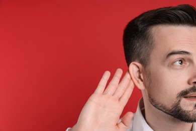 Photo of Man showing hand to ear gesture on red background, closeup. Space for text