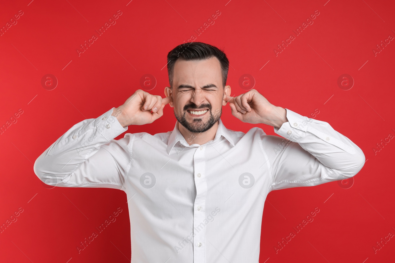 Photo of Man covering his ears with fingers on red background