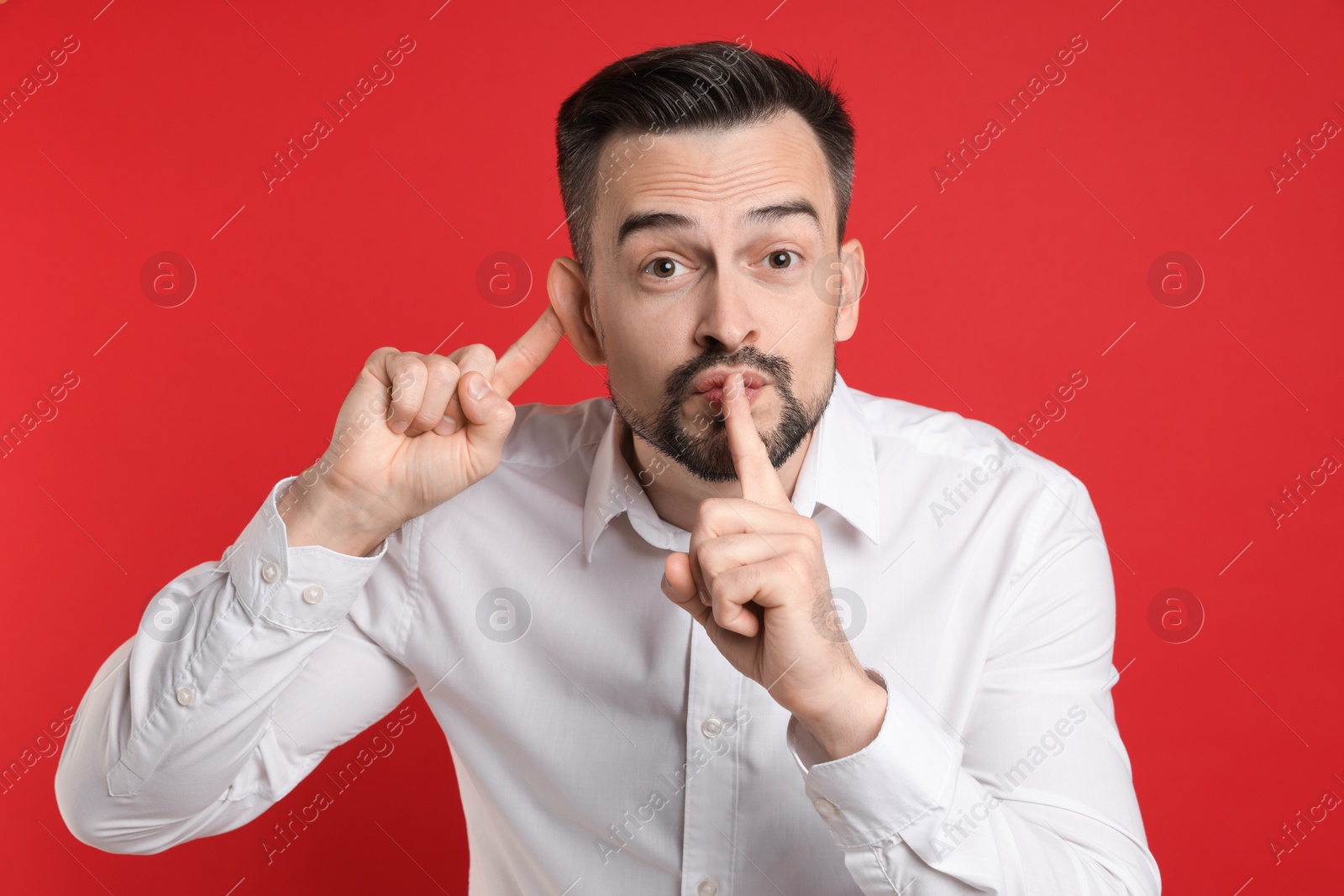 Photo of Man showing hand to ear gesture on red background