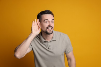 Photo of Man showing hand to ear gesture on orange background