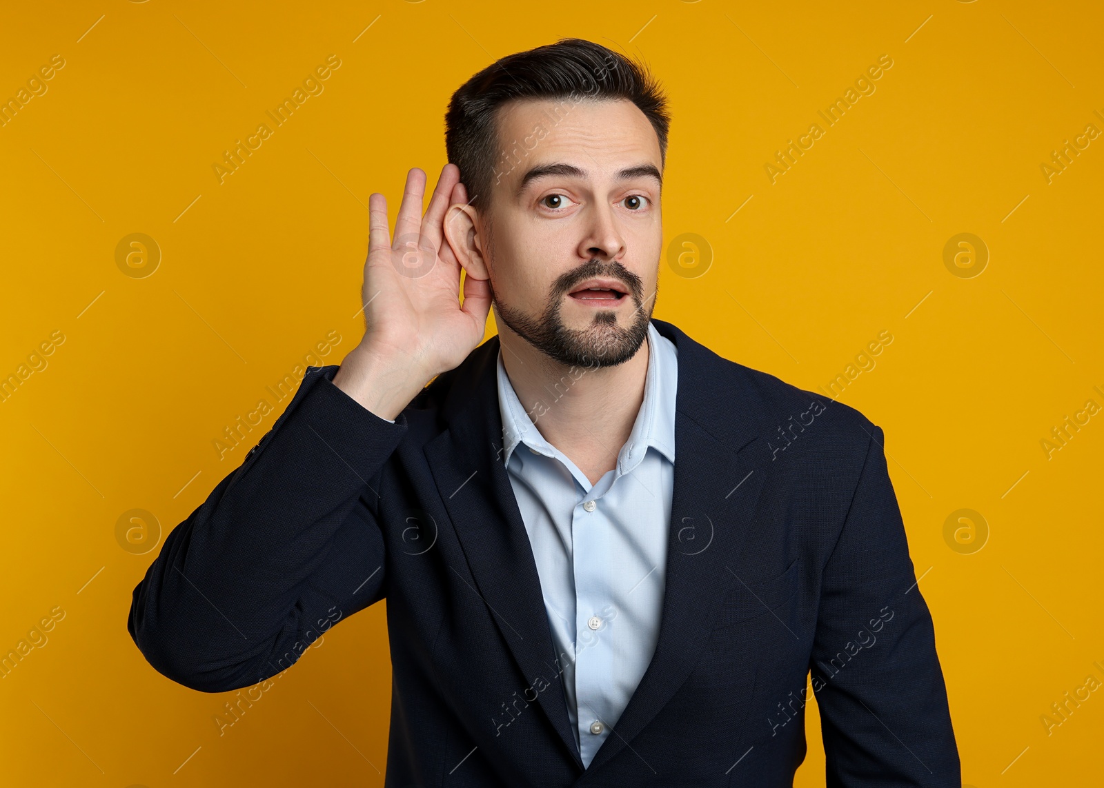 Photo of Man showing hand to ear gesture on orange background