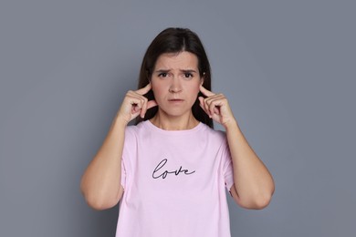 Photo of Woman covering her ears with fingers on grey background