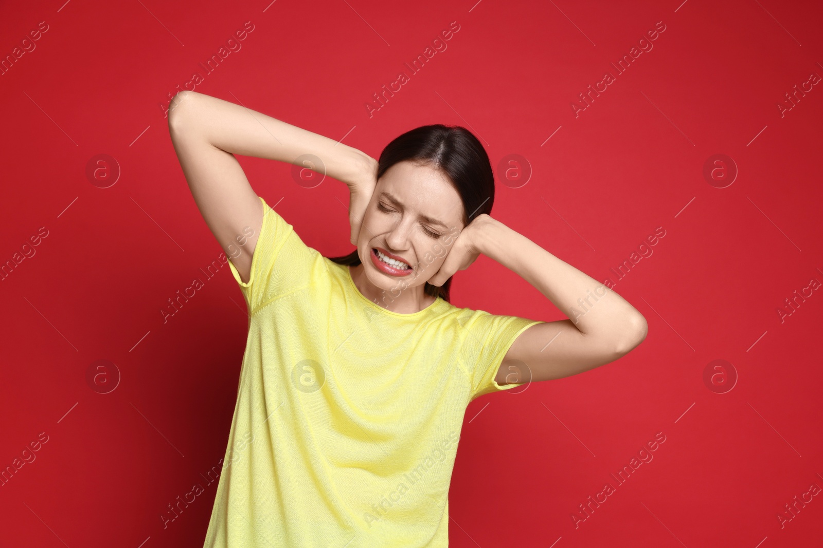 Photo of Woman covering her ears on red background