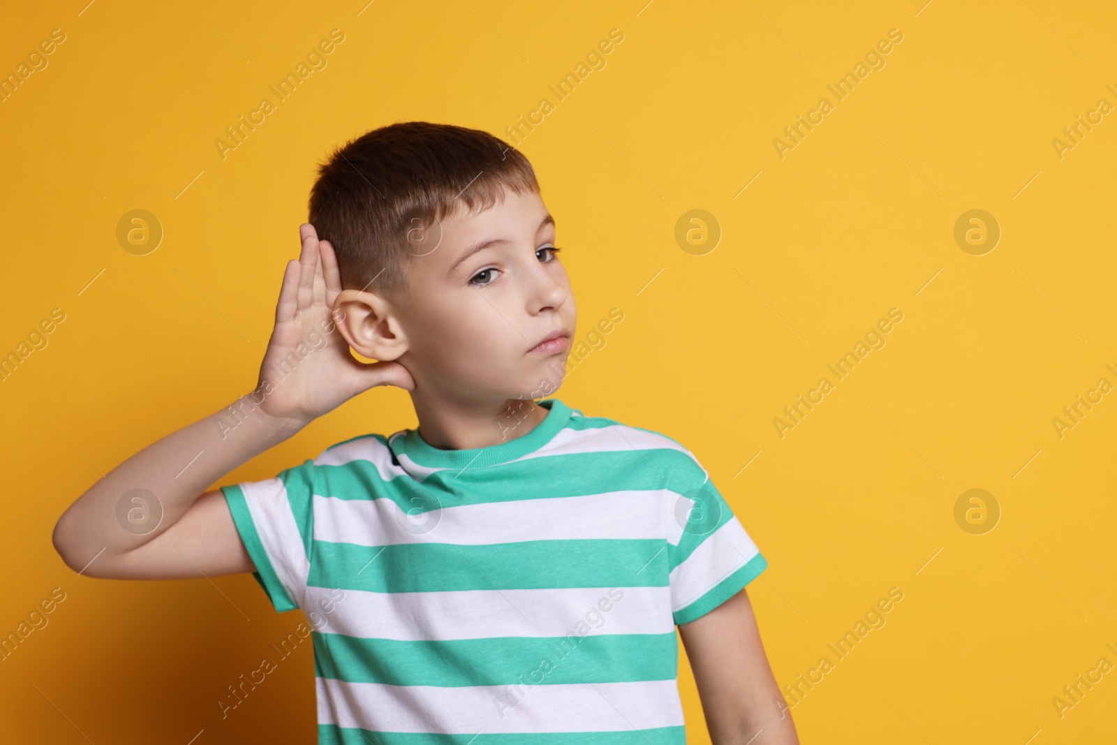 Photo of Little boy showing hand to ear gesture on orange background