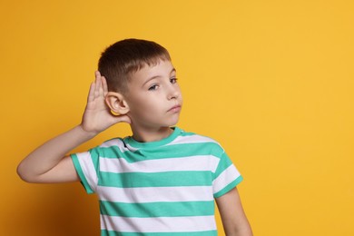 Photo of Little boy showing hand to ear gesture on orange background