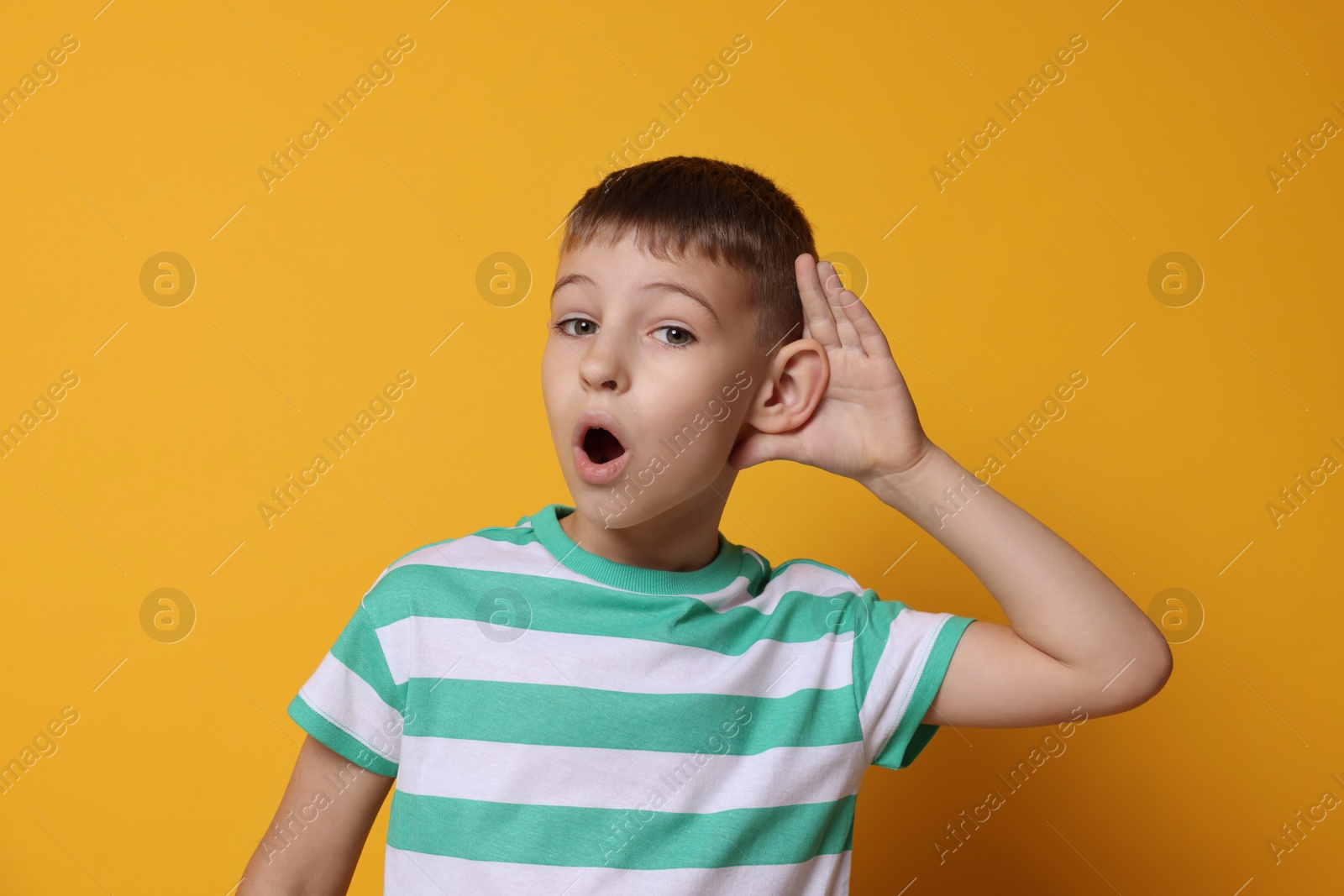 Photo of Little boy showing hand to ear gesture on orange background