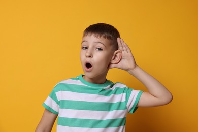 Little boy showing hand to ear gesture on orange background