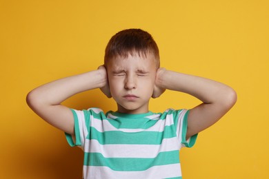 Little boy covering his ears on orange background