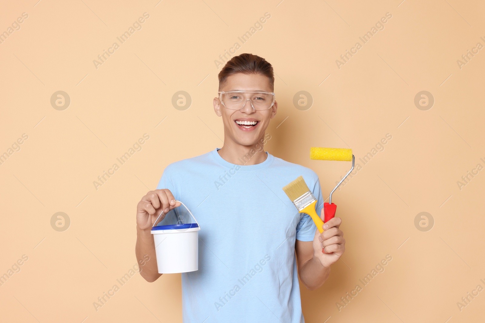 Photo of Portrait of young decorator with different tools on beige background