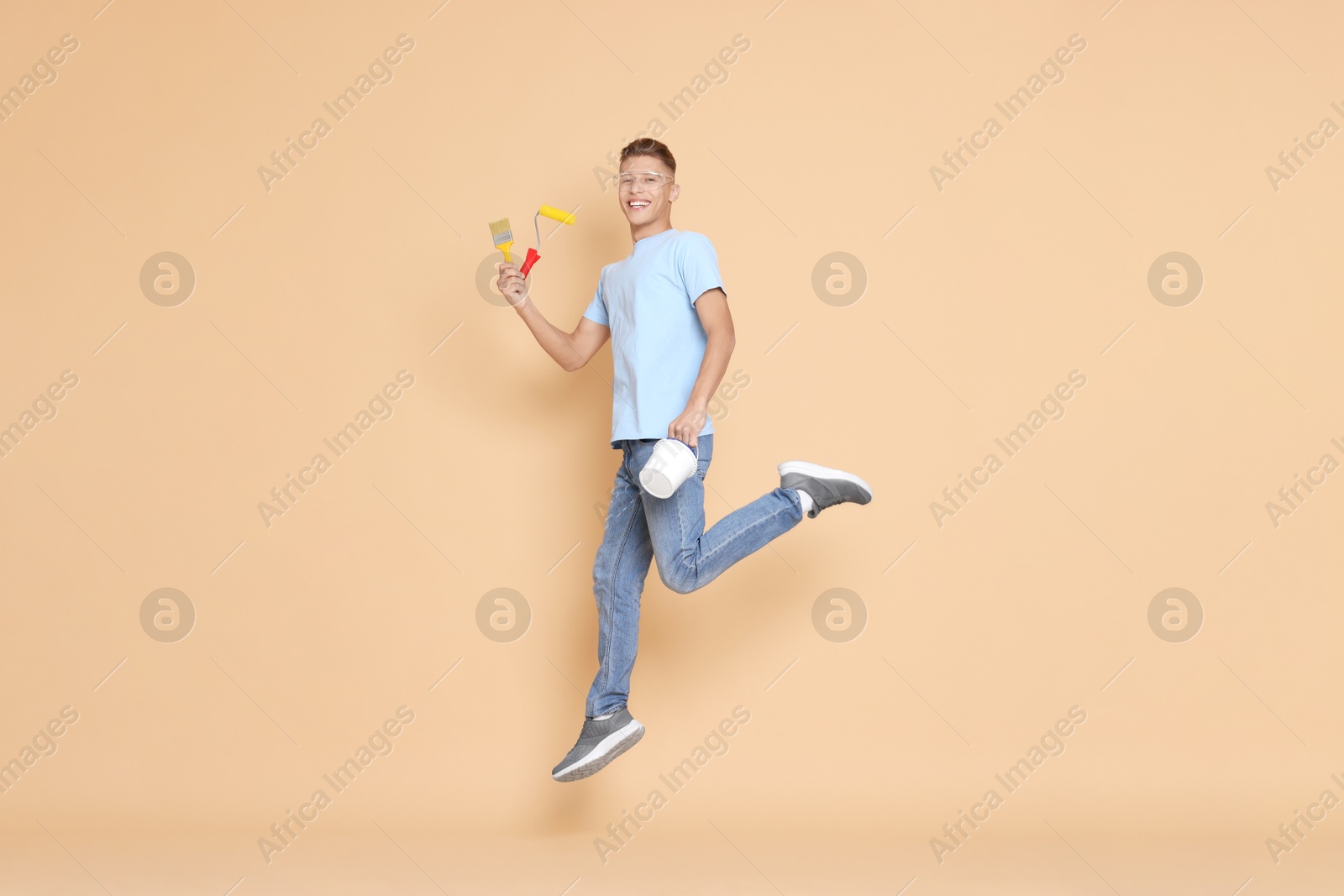 Photo of Young decorator with tools jumping on beige background