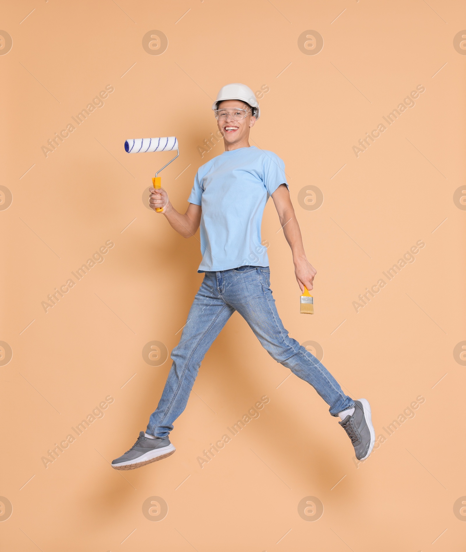 Photo of Young decorator with tools jumping on beige background