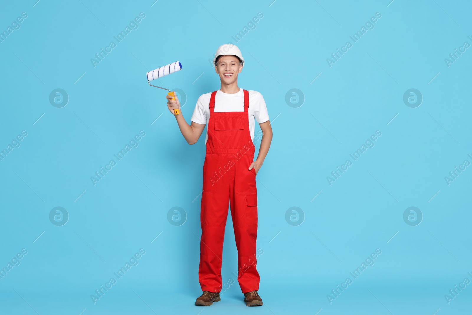 Photo of Young decorator with paint roller on light blue background