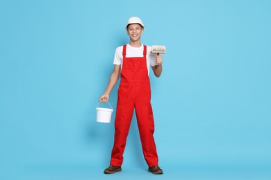 Photo of Young decorator with bucket and brush on light blue background