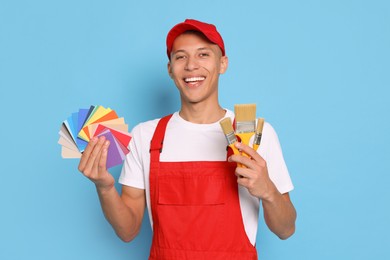 Photo of Portrait of young decorator with color palettes and brushes on light blue background